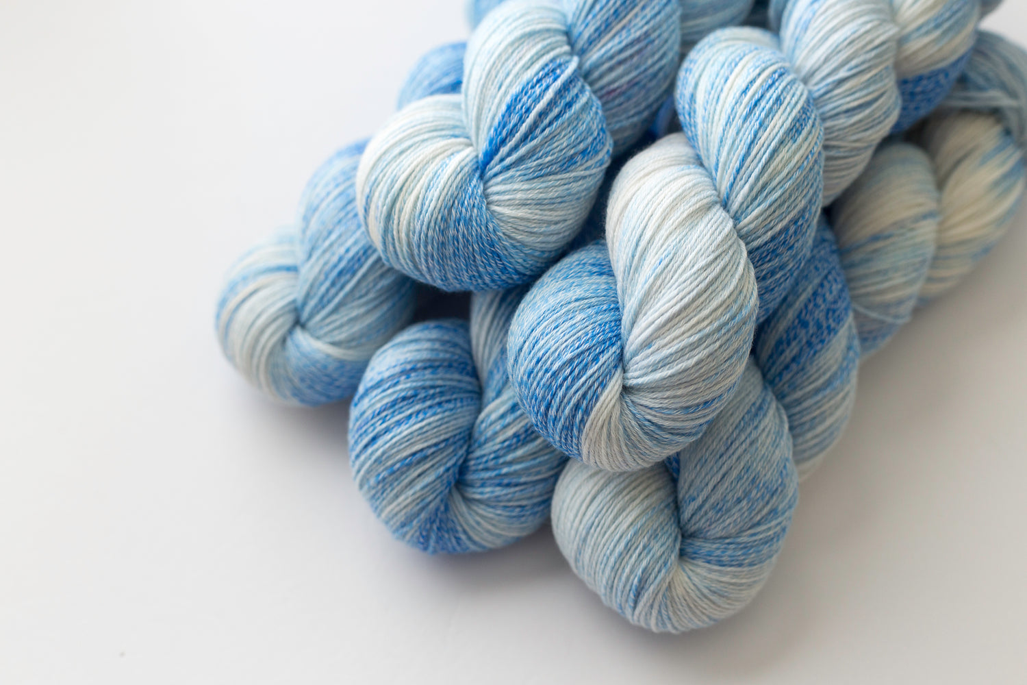 Clear Sky merino cotton knitting yarn.  A close-up of several skeins of variegated yarn in shades of light blue, medium blue, and white, arranged on a plain white background.