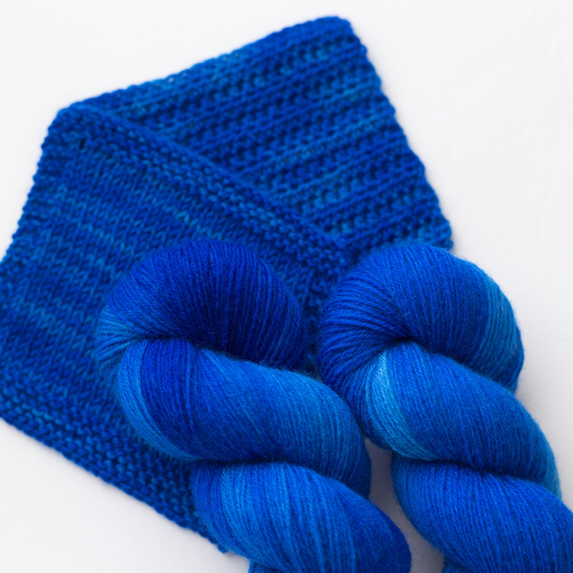 Vibrant blue BFL yarn laying atop a knitted swatch and a crochet swatch.