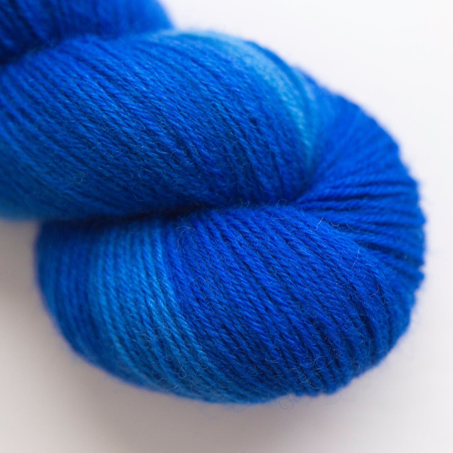 A close-up of a skein of blue faced Leicester yarn in a rich blue color, showing the soft texture of the plied fibers against a clean white background.