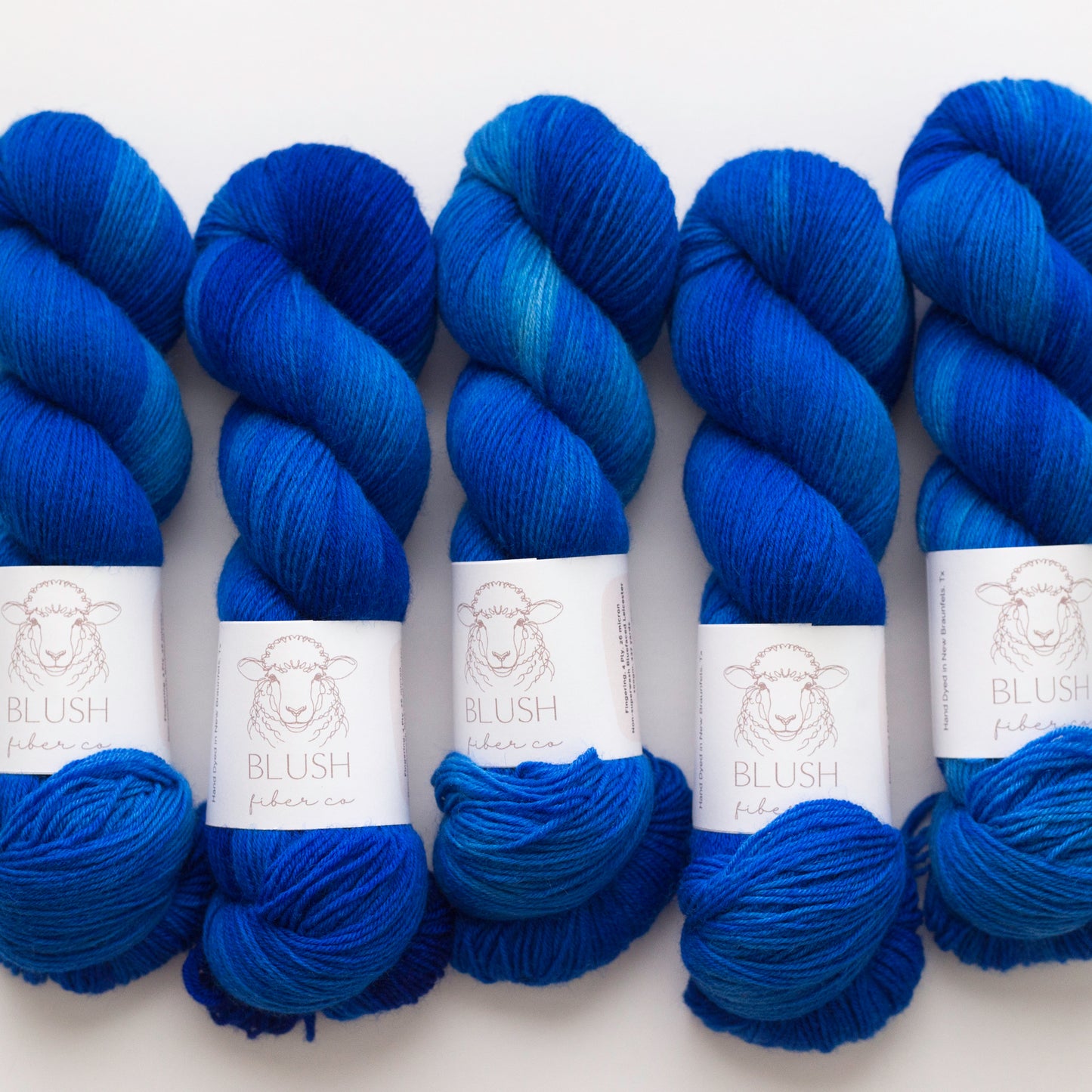 Five skeins of yarn in a rich blue-violet gradient, arranged side-by-side on a plain white background. Each skein has a white paper label with a sheep illustration and the brand name 'BLUSH fabric co.