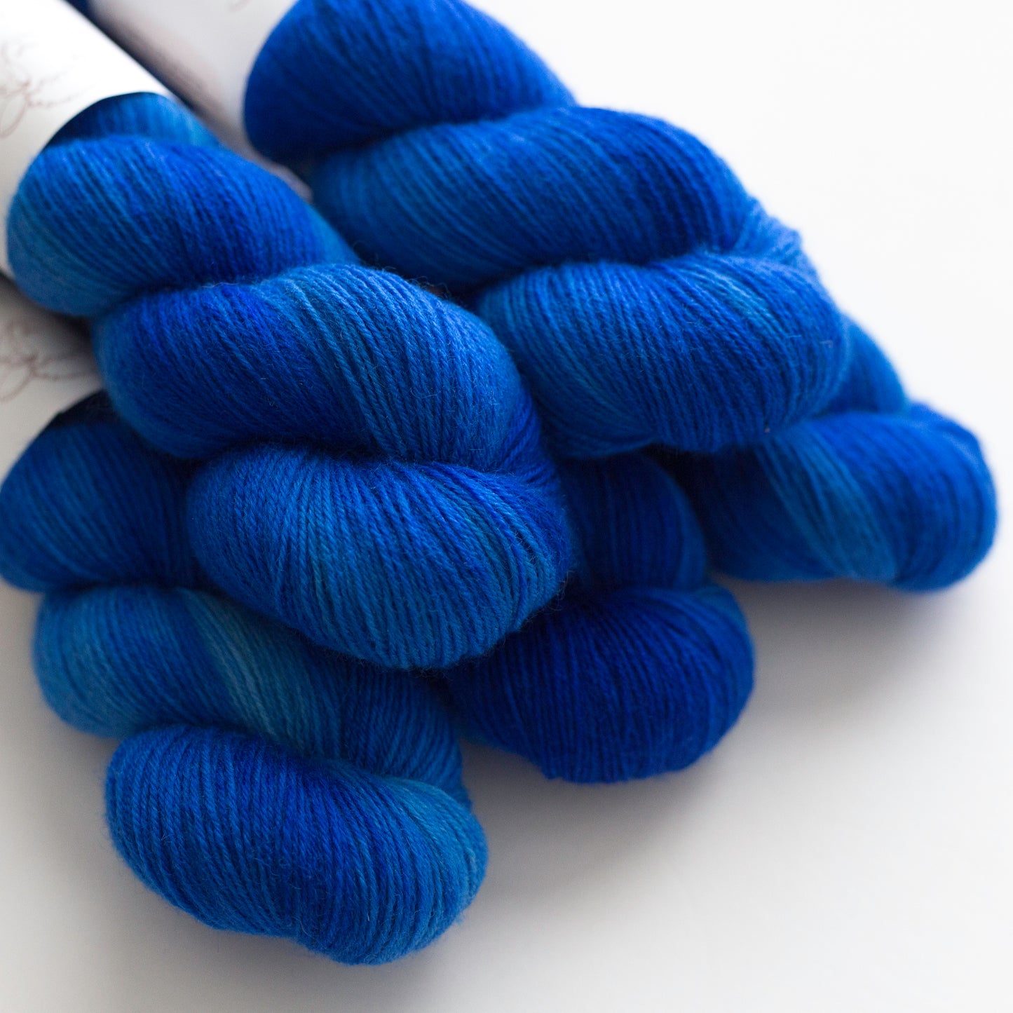 A close-up of several skeins of knitting yarn in a rich gradient of deep blue , resting on a clean white surface.